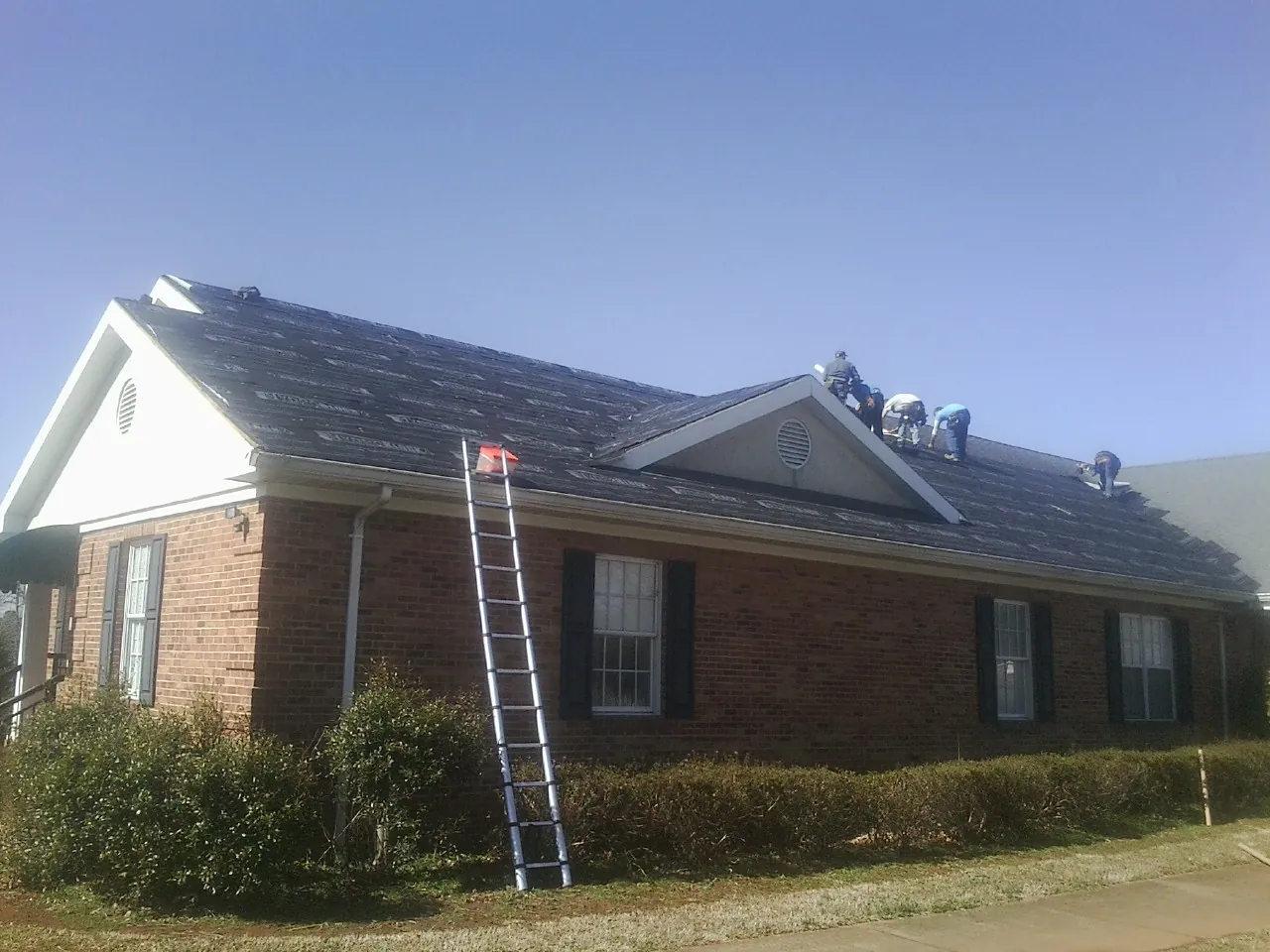 Crew tearing shingles off a brick ranch roof with a ladder set — Emergency Roof Repair work by our crew in Dresden