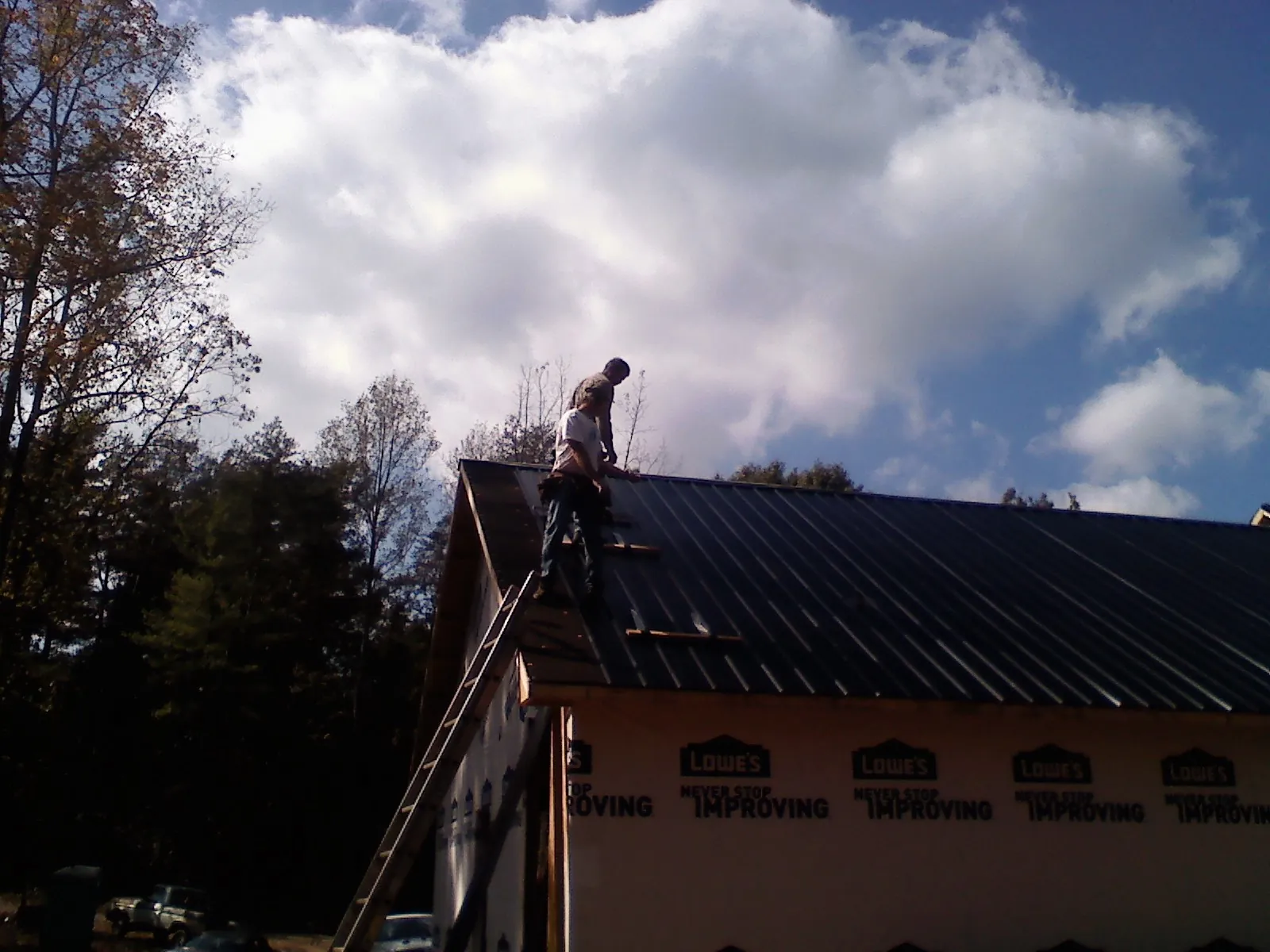 Roofer fastening dark metal panels high against a cloudy sky, from a Roof Inspection job in Dresden