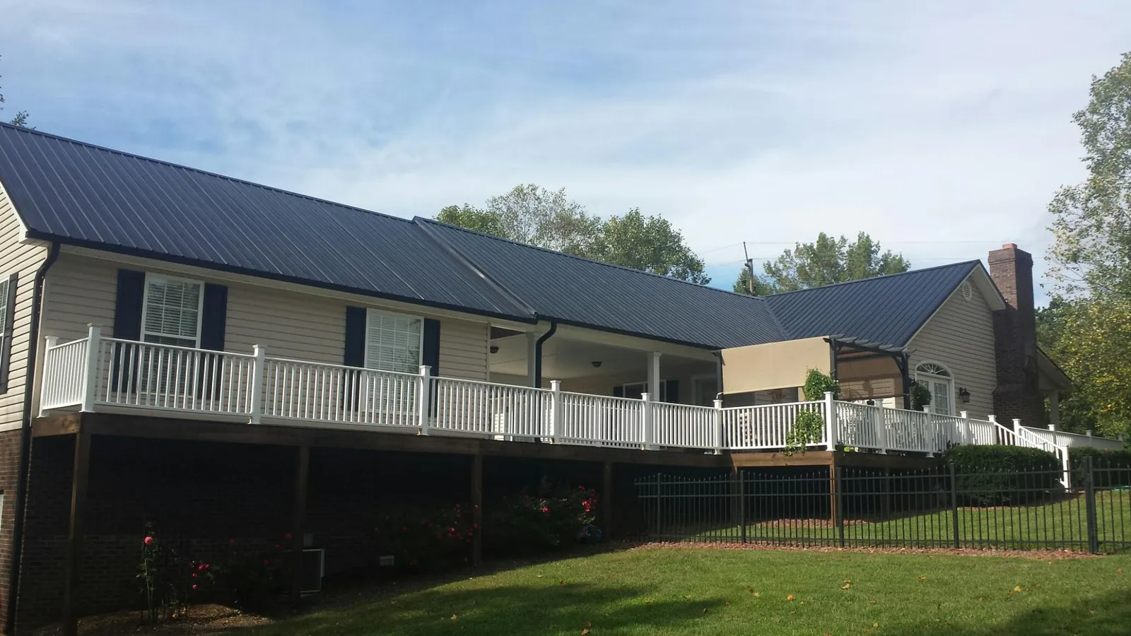 Black metal roof above a long white railed deck on a hillside home in Dresden